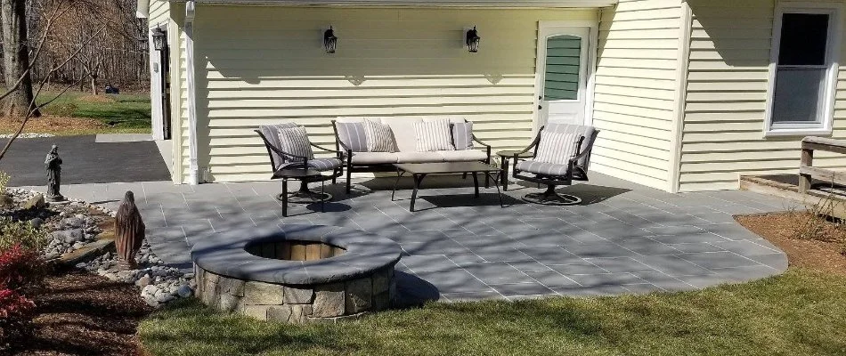 A patio attached to a house in Bristow, VA, with a fire pit, table, and chairs.