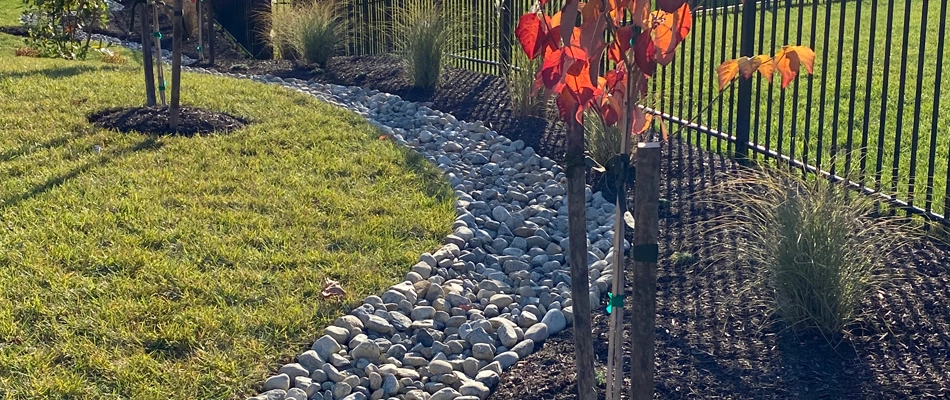 Dry creek bed on a residential property next to a landscape bed and fence.
